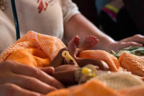 Ett nyfött barn insvept i en filt ligger framför en anställd på en klinik i Sydsudan