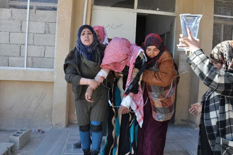 Några kvinnor stöttar en kvinna med dropp utanför en vårdcentral i Abu Qalqal, Syrien.