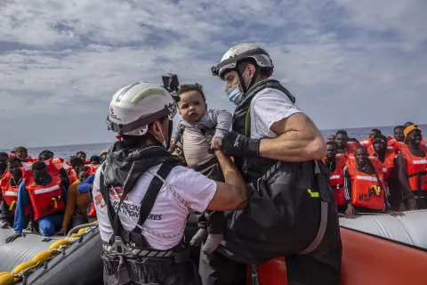 Två medarbetare från Läkare Utan Gränser lyfter upp en liten pojke ur en gummibåt på centrala Medelhavet.