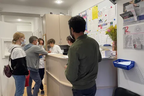 Personer står i kö vid receptionen på en vårdcentral