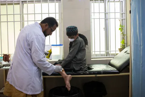 En pojkes sår på benet rengörs av en läkare. Pojken har även bandage på näsan.
