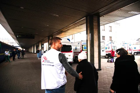 En man i Läkare Utan Gränser väst leder två kvinnor mot ett tåg
