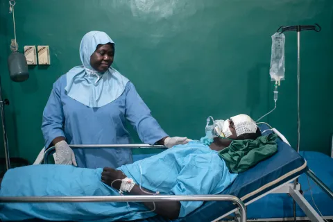 En sjuksköterska i operationskläder tar hand om en patient i en sjukhussäng