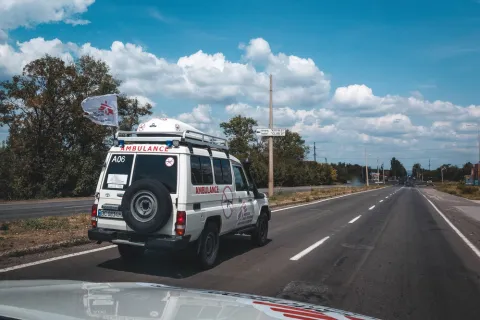 En ambulans med en flagga med Läkare Utan Gränsers logga på en rak asfalterad väg. 