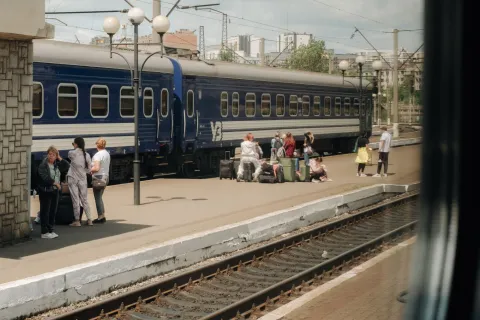 Tågräls och ett tåg med människor som väntar med väskor på perrongen.