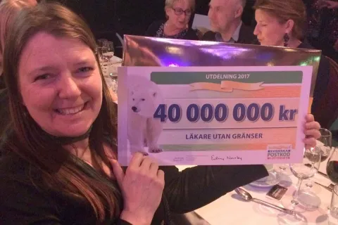 En kvinna håller upp en jättestor check från Postkodlotteriet